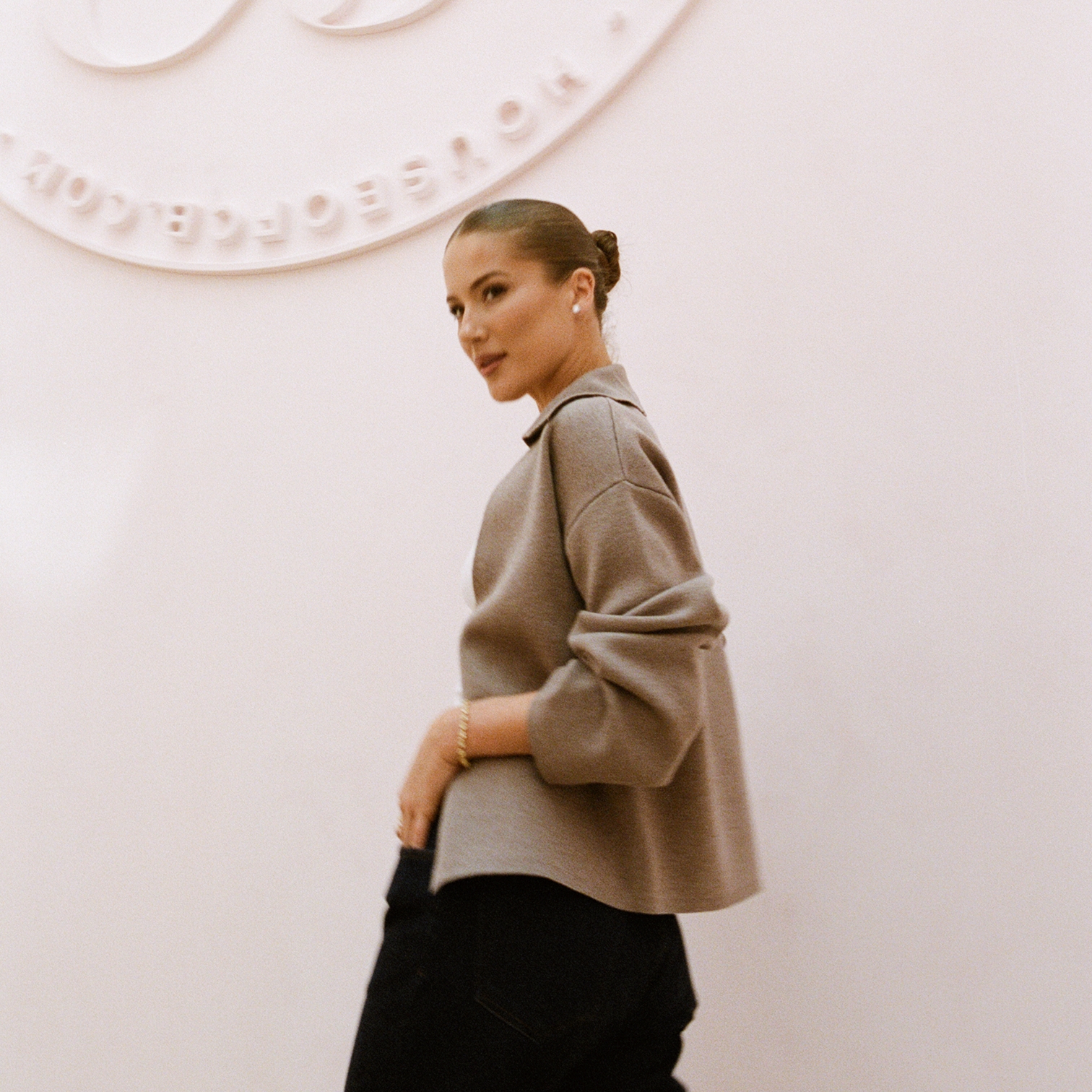 Conna Walker, House of CB founder, in a taupe collared knit jacket against the embossed wall seal